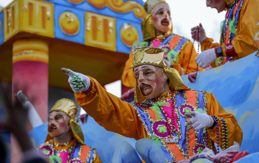Float rider in full Mardi Gras costume throwing beads from a vibrant parade float during a New Orleans Mardi Gras celebration.